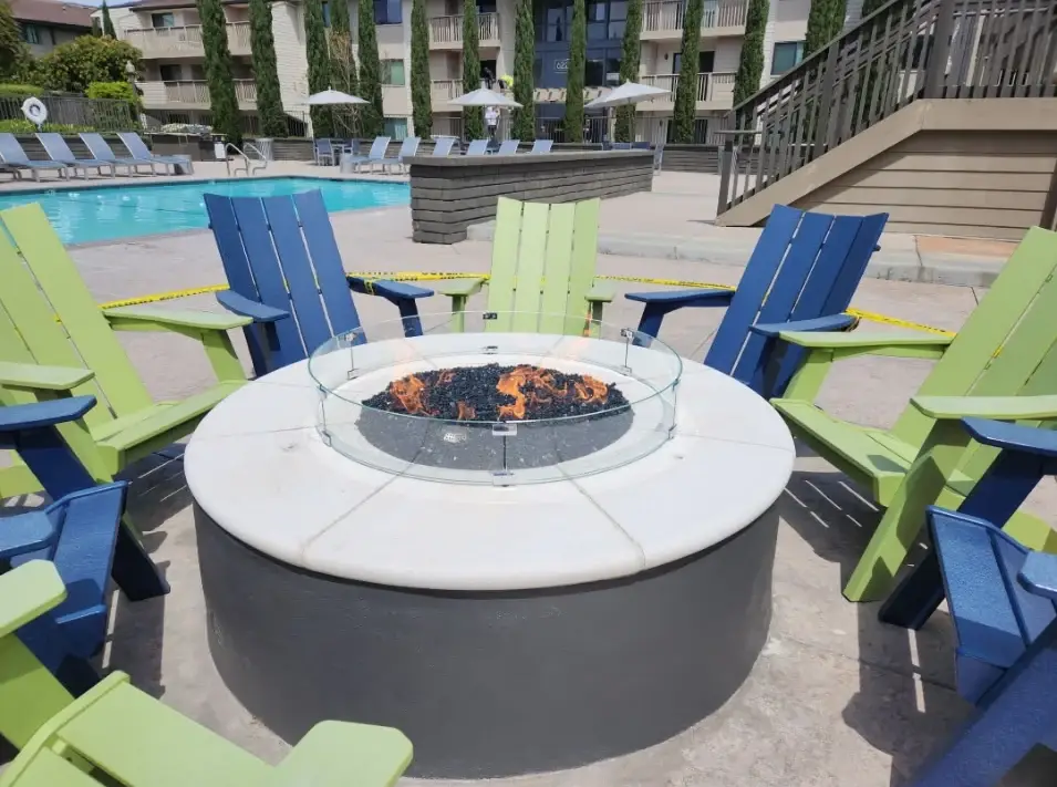 Round firepit surrounded by adirondack chairs near pool