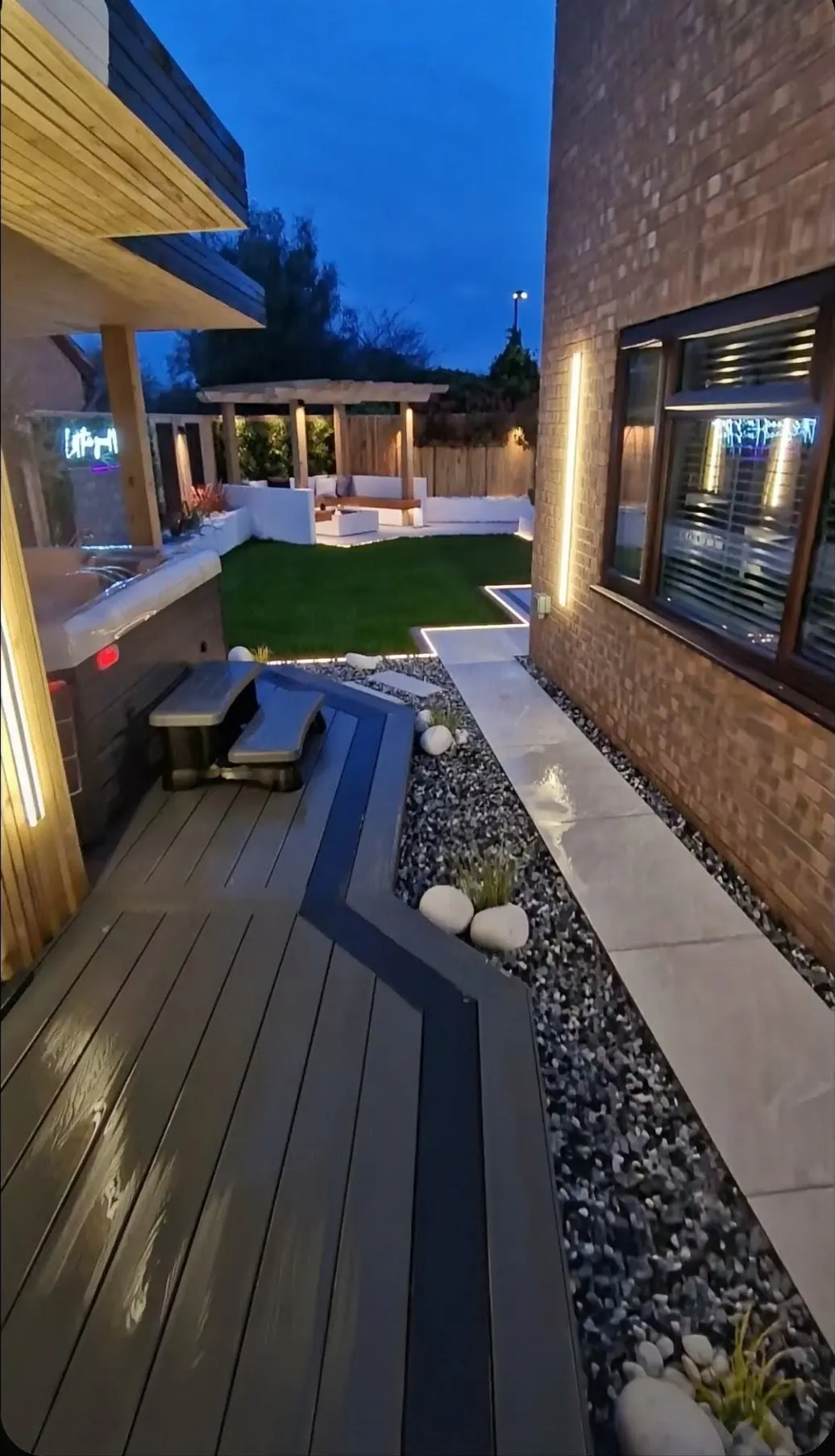 Backyard outdoor living room with composite deck, sectional, and warm uplighting at dusk